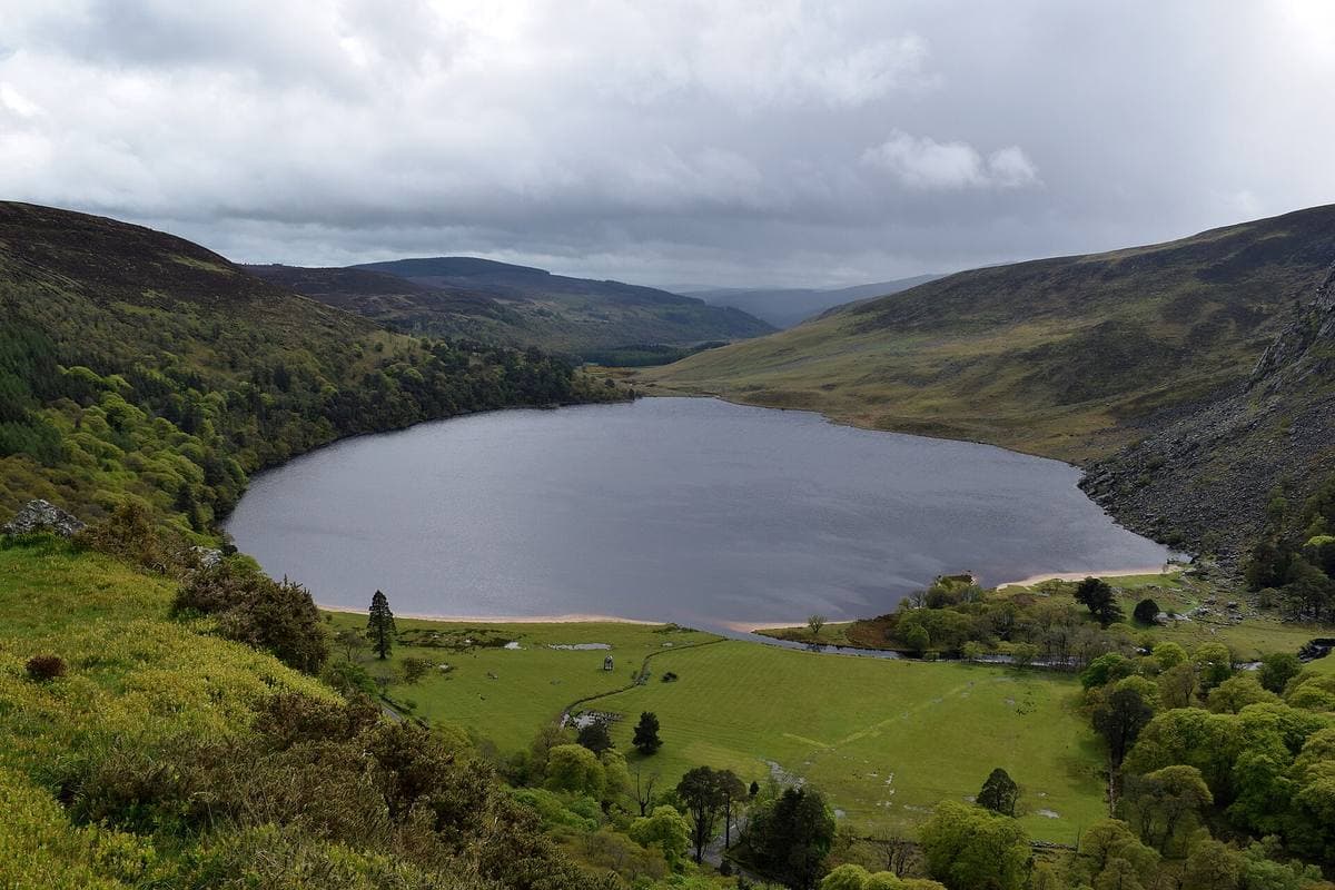 A dark lake in a steep green valley with a pale beach at its near end