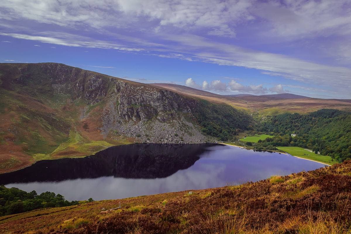 A long dark lake under steep cliffs, heather in the foreground