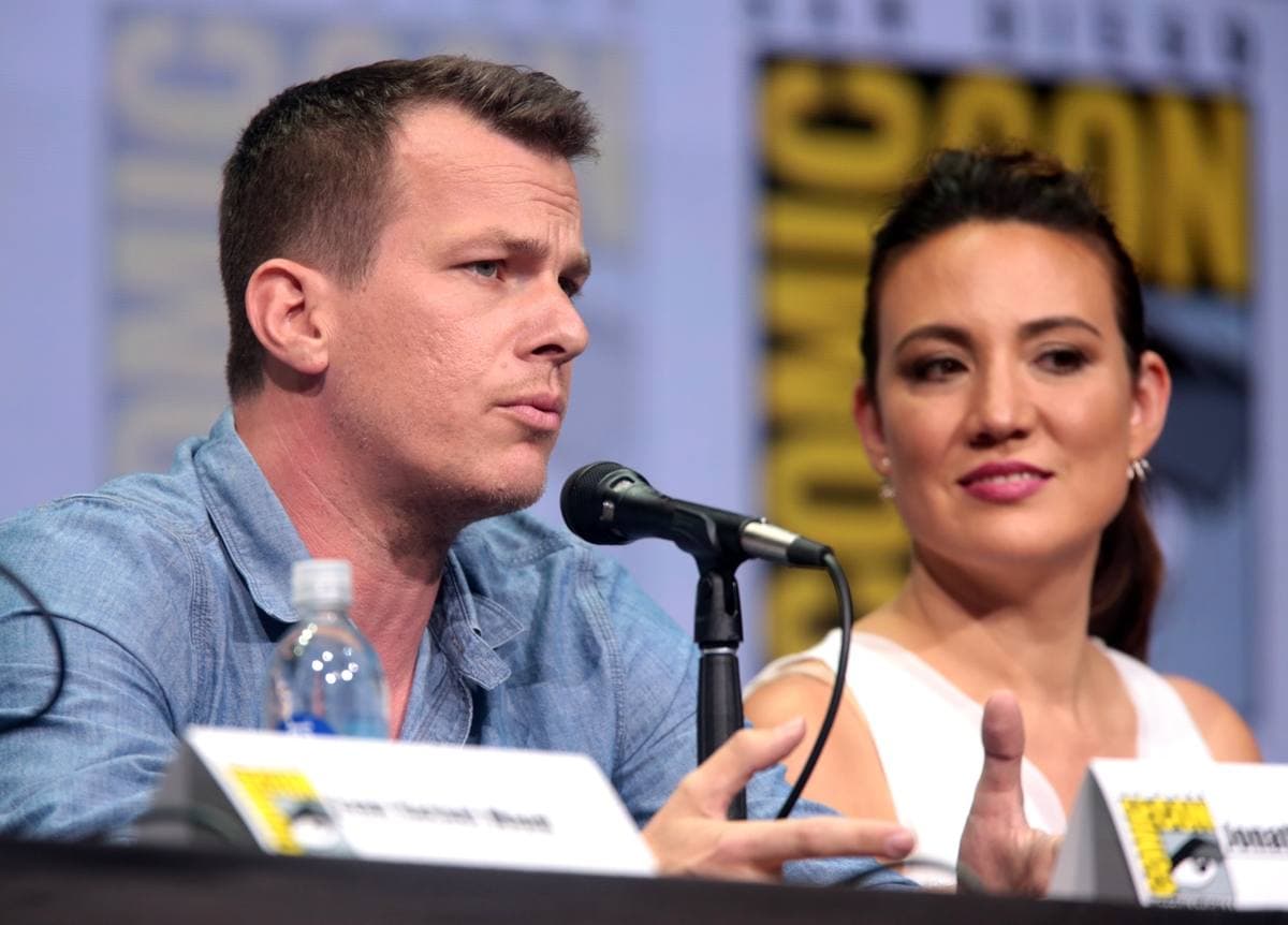 Jonathan Nolan speaking into a microphone beside Lisa Joy