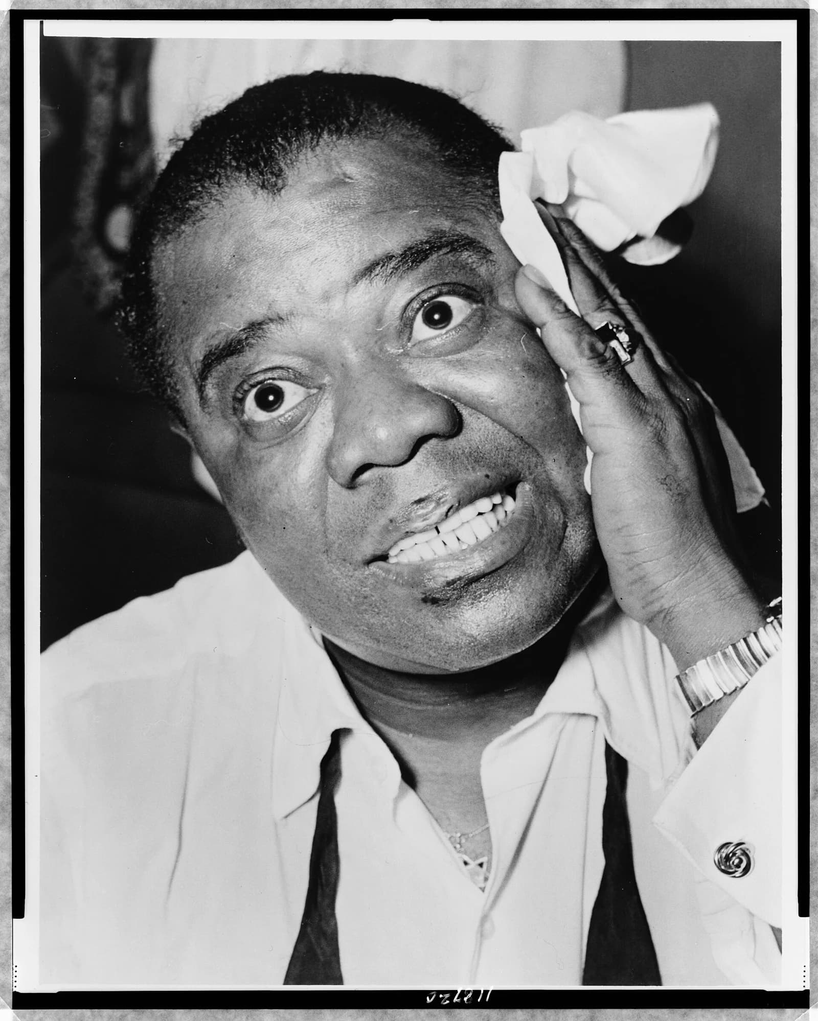 Louis Armstrong smiling and holding a handkerchief beside his face