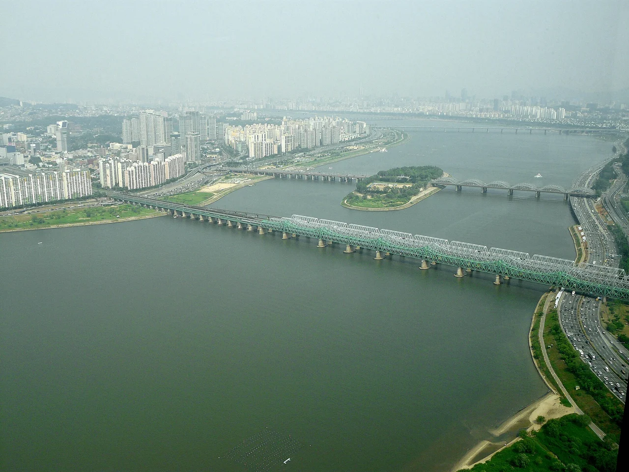 The green steel trusses of the Hangang Railway Bridge crossing the Han River towards Nodeul Island, seen from high above Yeouido