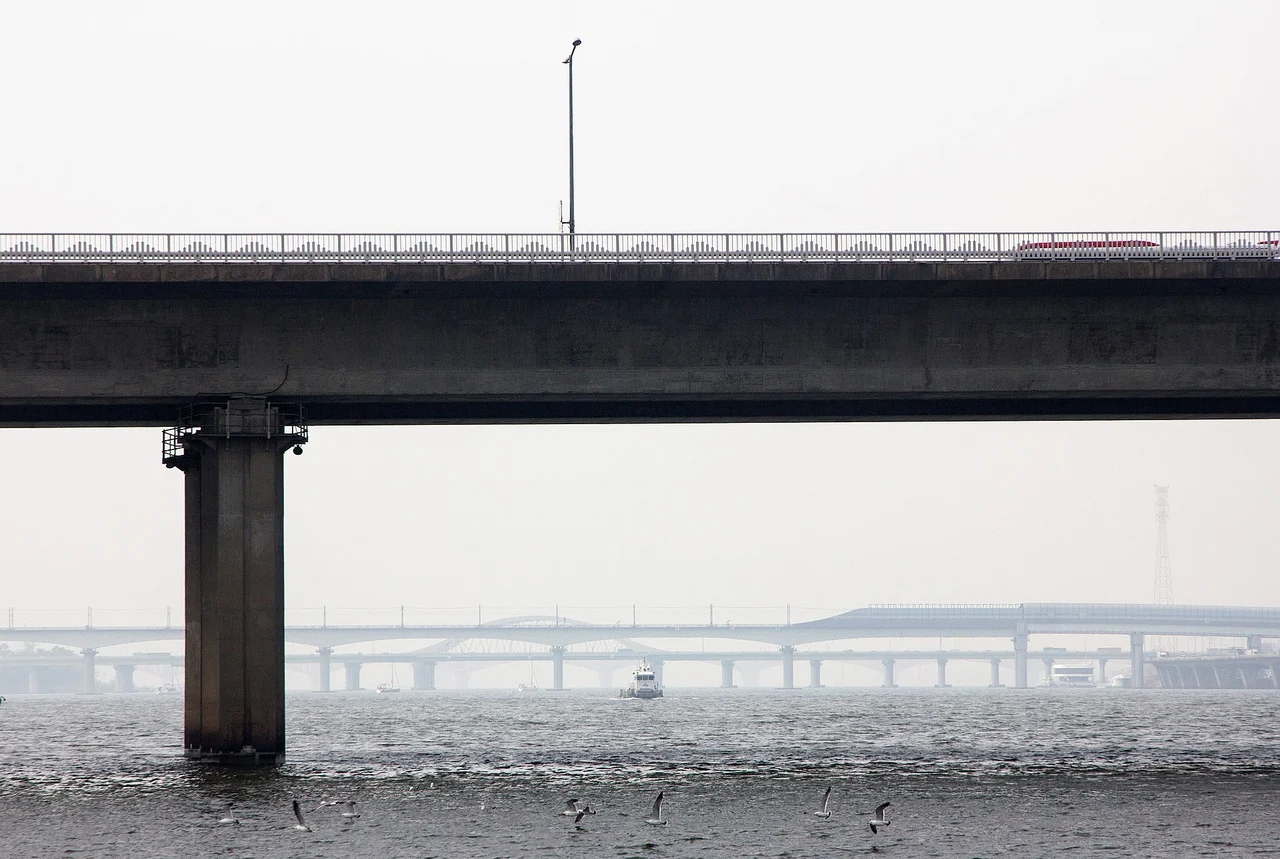 The concrete deck and a pier of Seogang Bridge over the Han River, with gulls over the water and more bridges in the haze beyond