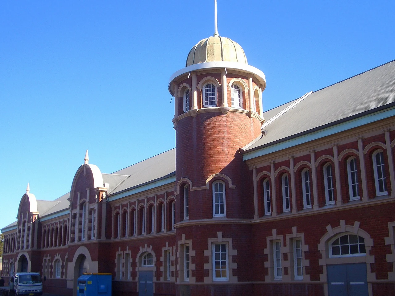 A long red-brick hall with a round domed tower under a blue sky
