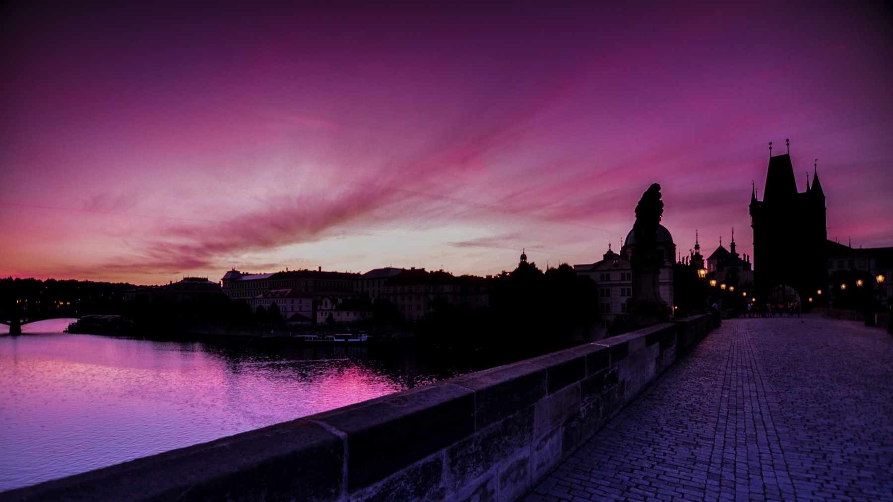 A stone bridge lined with statues under a pink dawn sky