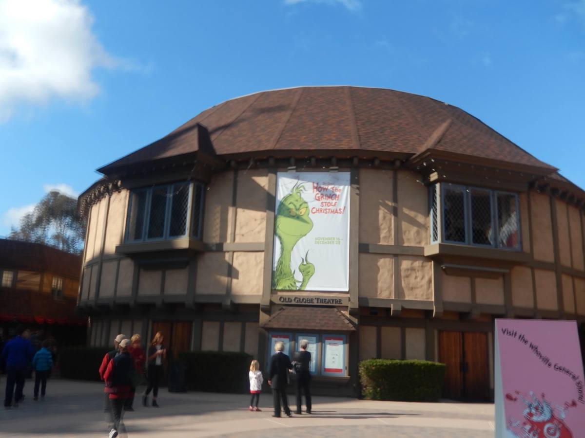 A timbered Tudor-style round theatre with a brown roof, with people walking in front