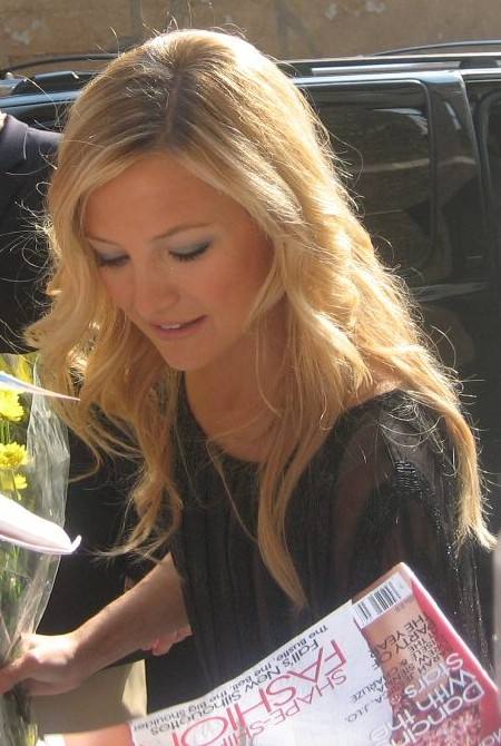 A young woman with long fair hair looks down as she signs a magazine