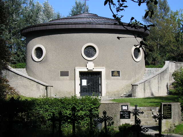 A round chapel behind a low wall, with iron grave crosses in front