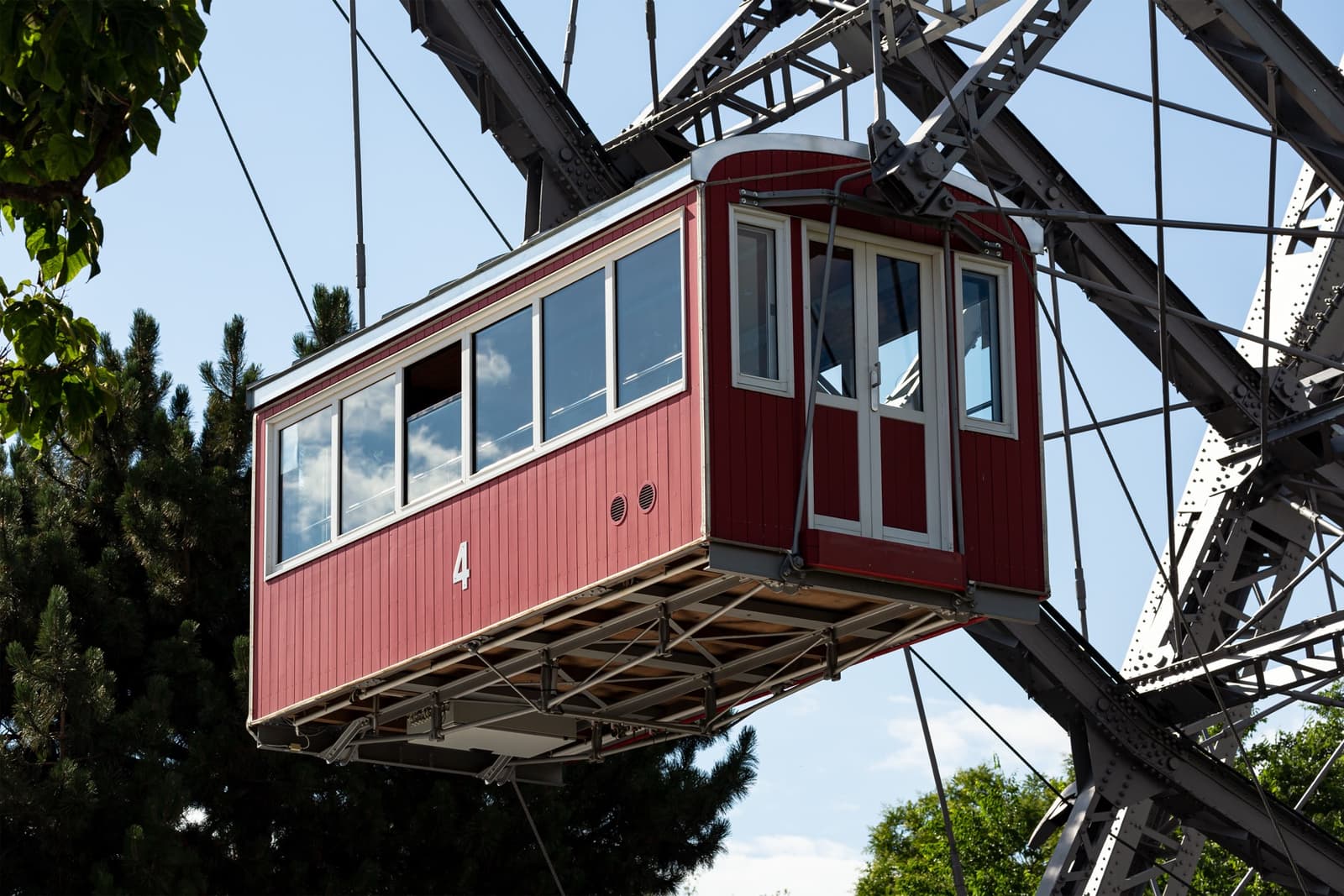 A red wooden Ferris-wheel cabin, numbered 4, hanging from the wheel’s iron spokes