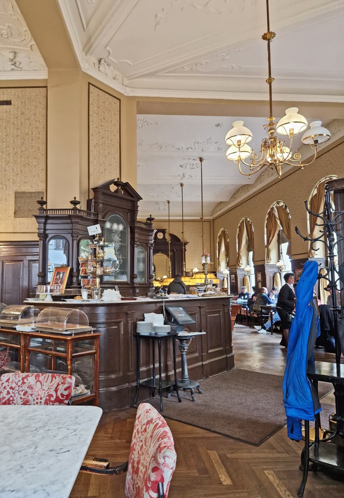 A Viennese café room with marble tables, wooden chairs and hanging lamps