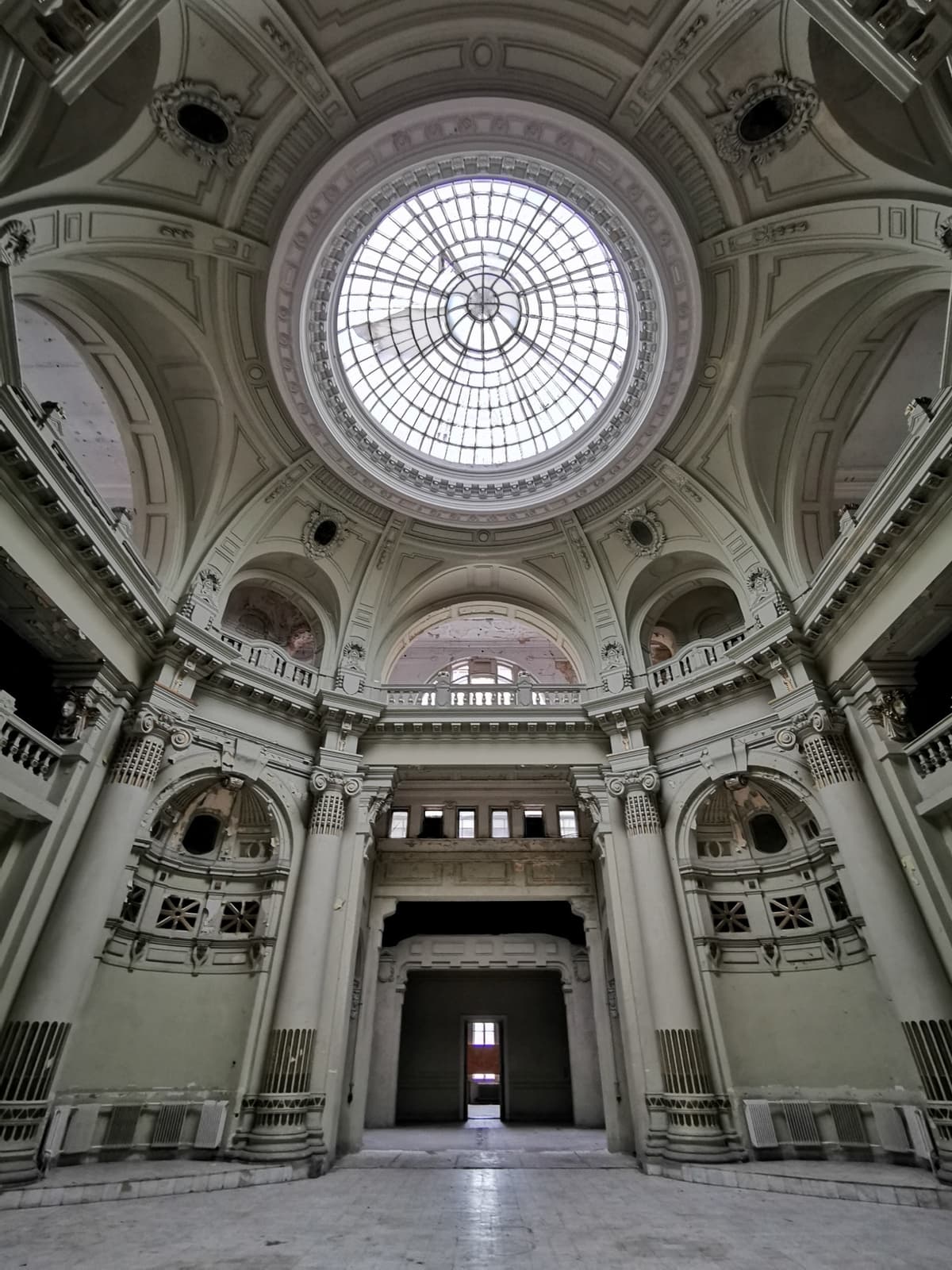 A grand domed stairwell with a round glass skylight and pale stone columns