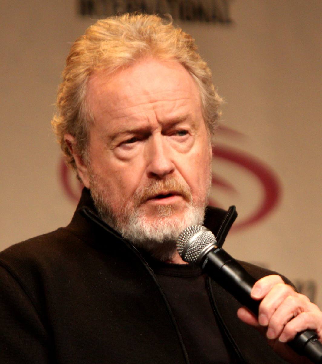 Ridley Scott, white-bearded, in a dark jacket, speaking into a microphone