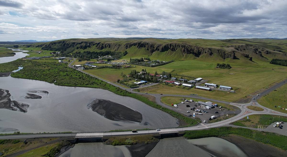 Aerial view of a small village beside a braided grey river and green cliffs