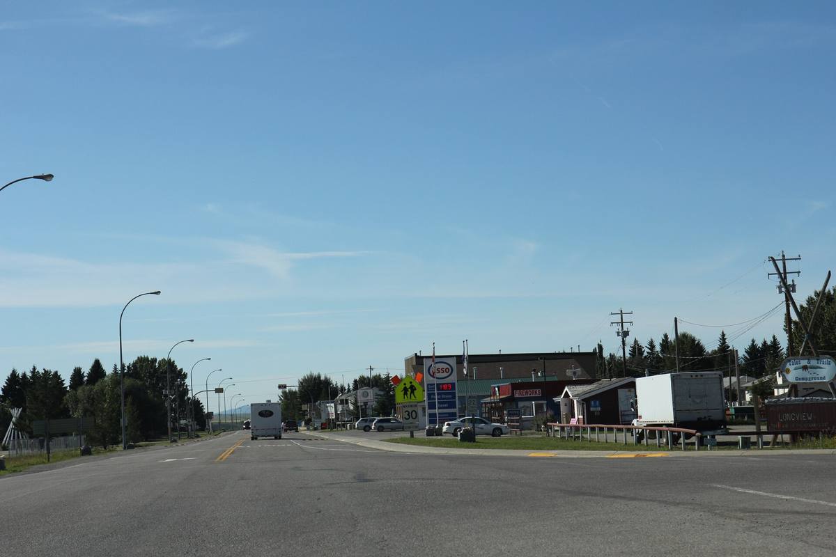 A small prairie village main road with low buildings and the foothills beyond