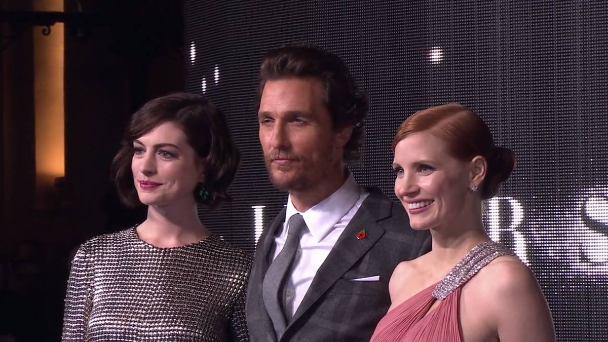 Anne Hathaway in a silver dress, Matthew McConaughey in a dark suit and Jessica Chastain in pink, standing together at a premiere
