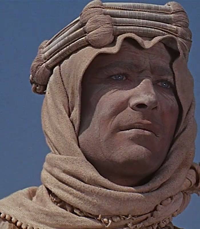Peter O’Toole in a sand-coloured headcloth against a deep blue sky, looking into the distance