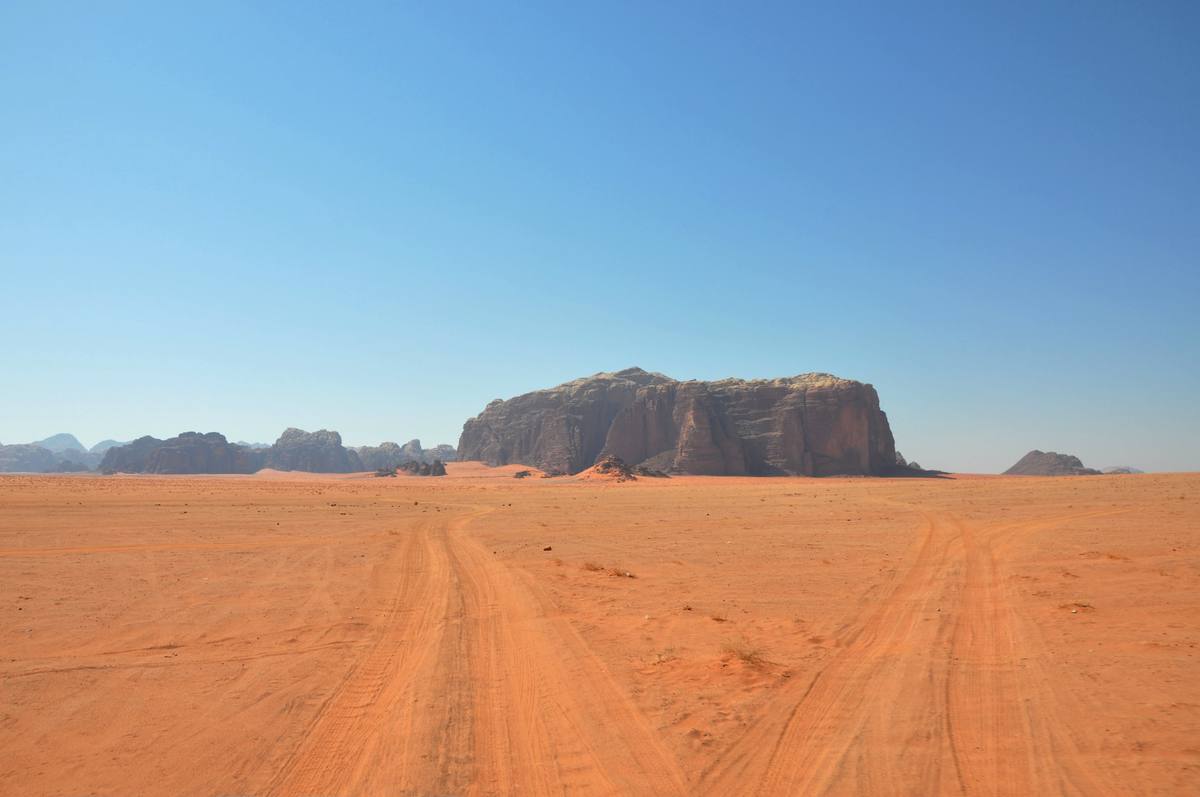 Two sets of jeep tracks running across red sand towards a flat-topped rock massif under a clear blue sky