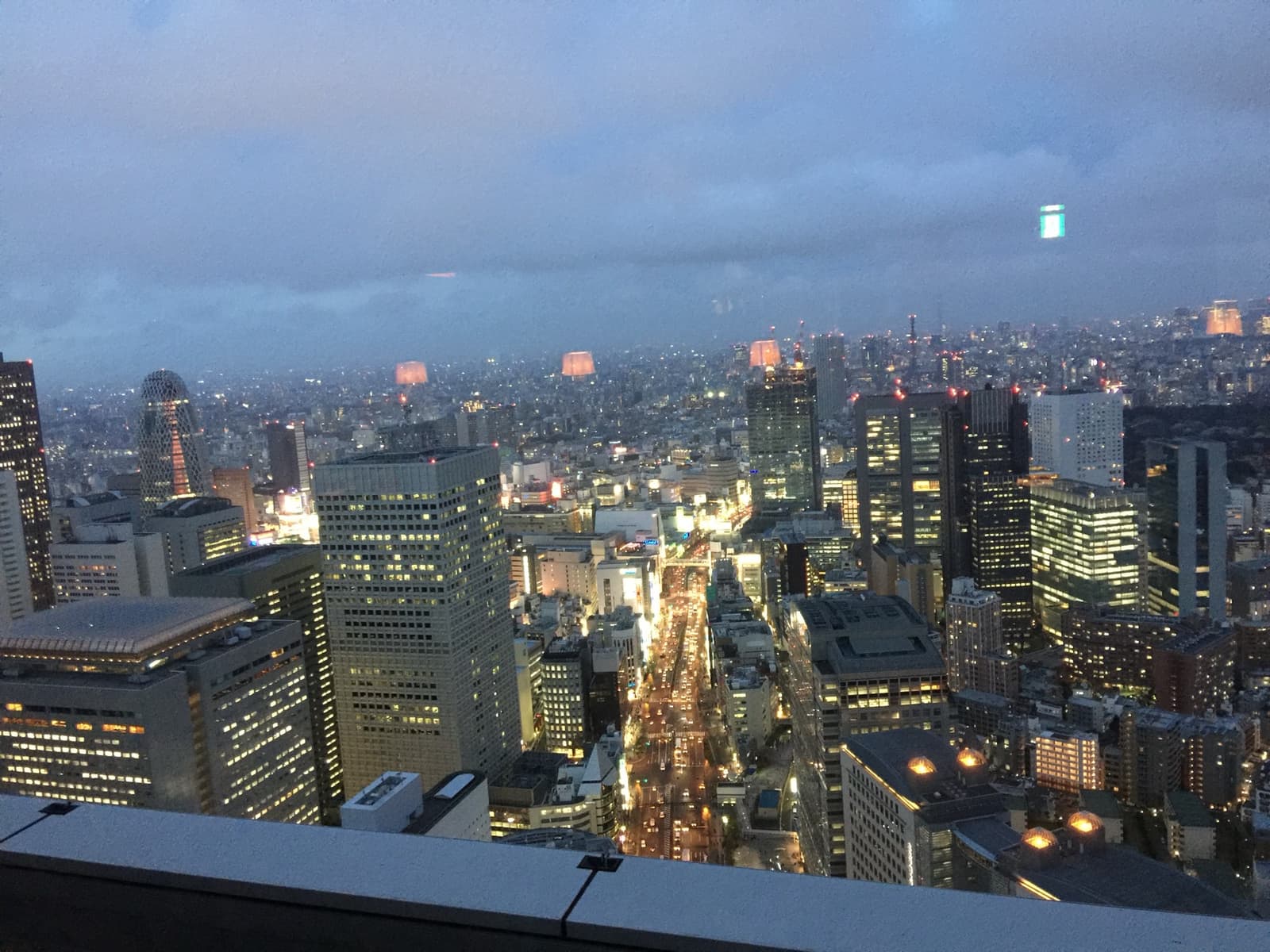 Night over Shinjuku from high up: office towers and a bright avenue running away