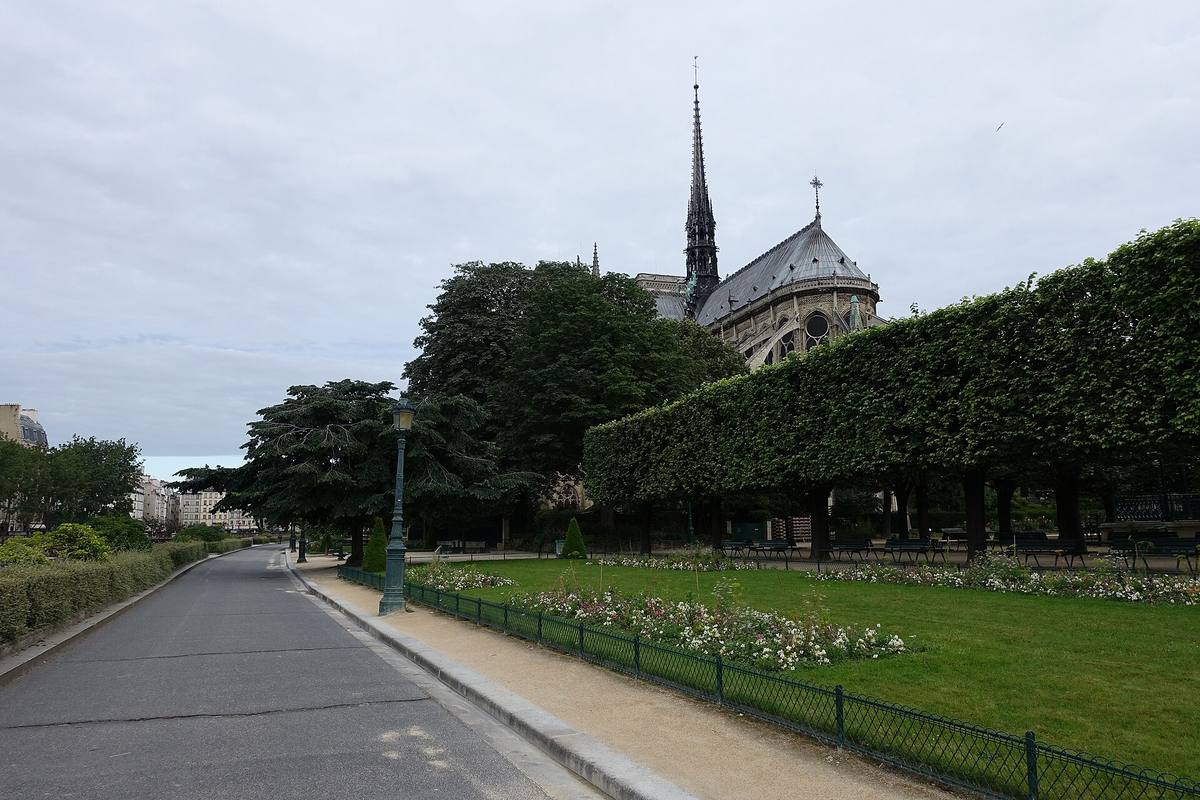 A tree-lined garden path with clipped hedges and lawns, Notre-Dame’s spire rising behind