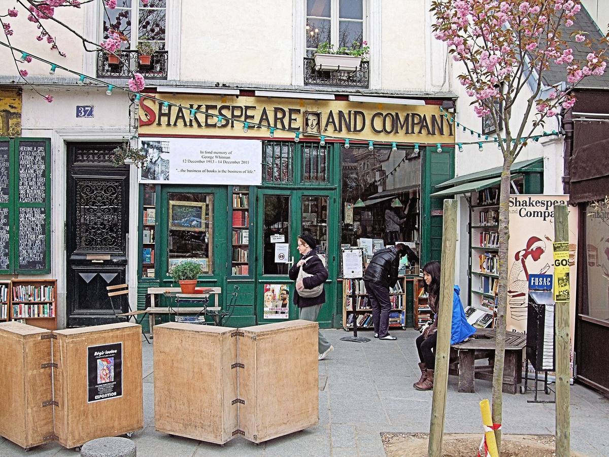 The green and yellow shopfront of Shakespeare and Company with book trolleys outside and a blossoming tree