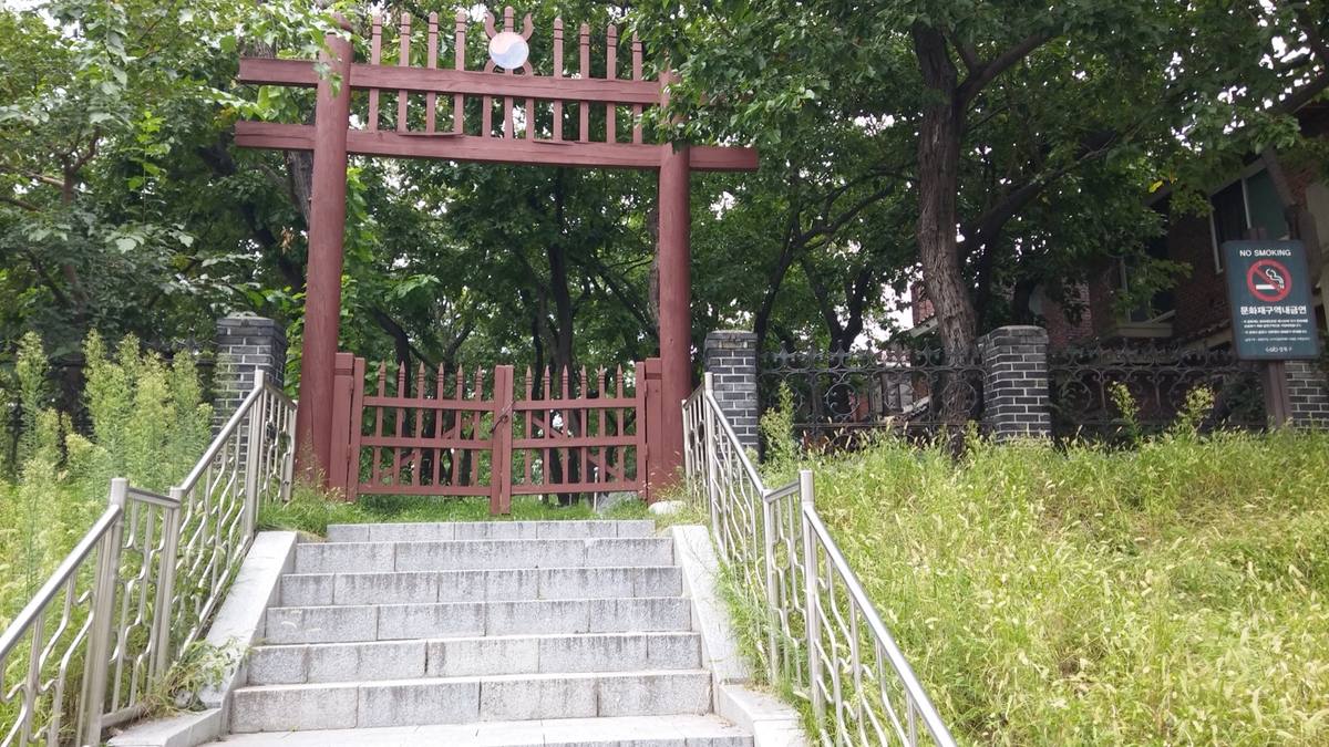 Colour photograph of steps leading up to a red wooden gate among trees