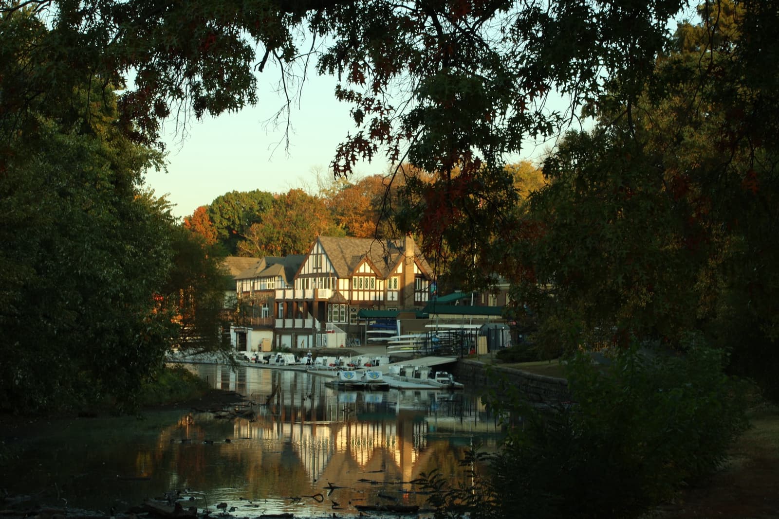 A Tudor-style boathouse reflected in the Schuylkill River at sunrise, framed by autumn trees
