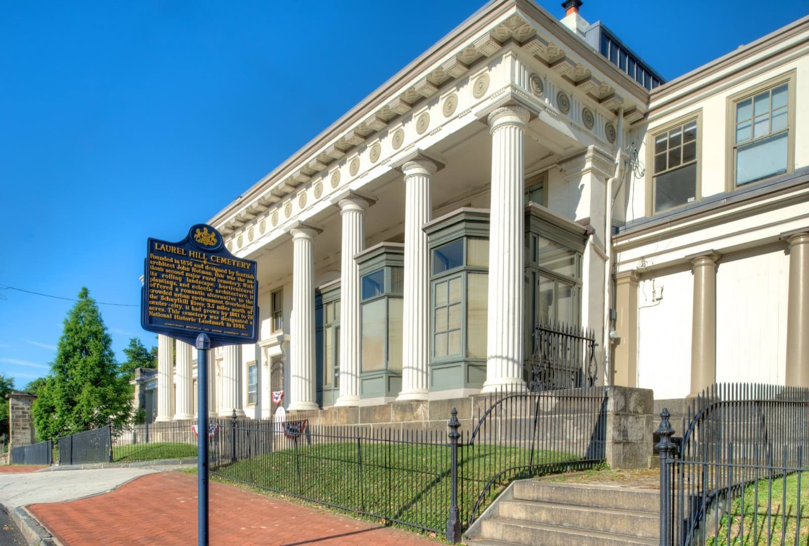 The columned stone gatehouse of Laurel Hill Cemetery under a blue sky