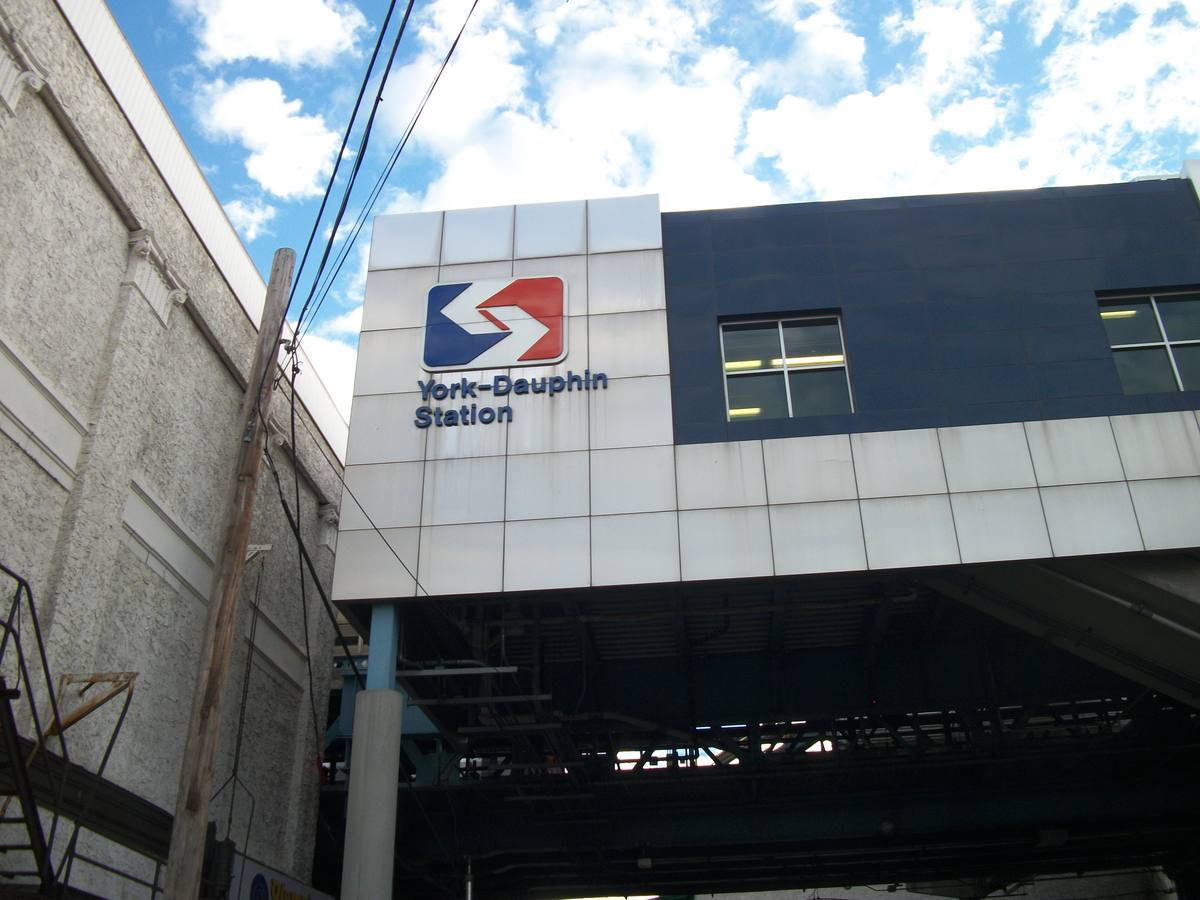 An elevated railway station clad in grey and blue panels, above the street on steel girders