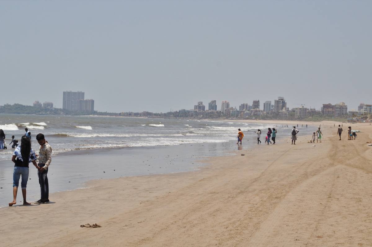 Colour photograph of a wide sandy beach with people walking at the water’s edge and tower blocks along the shore