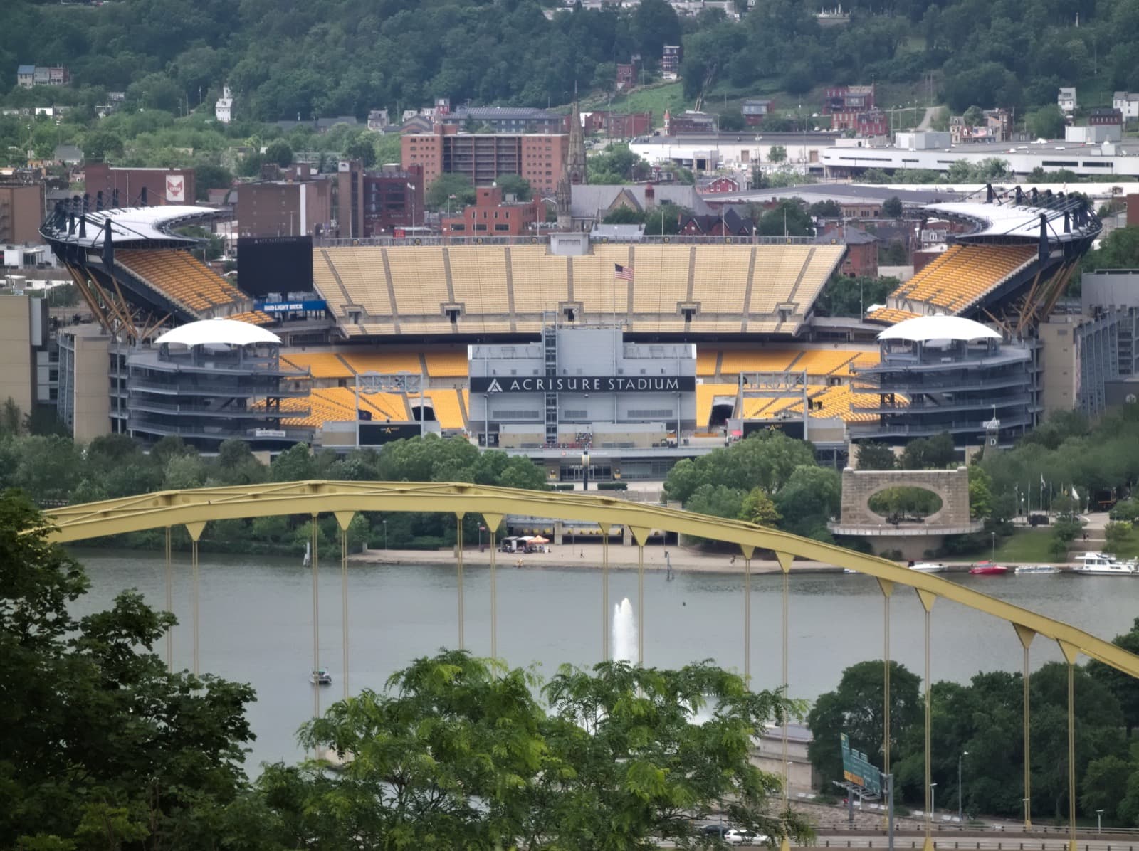 A yellow-and-black stadium across the river behind a steel bridge