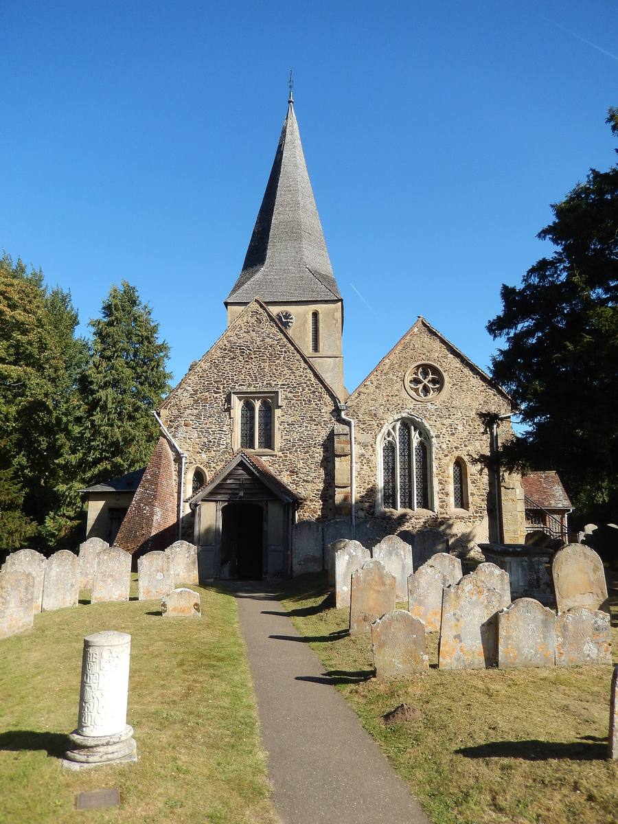 A flint church with a shingled spire at the end of a path through a churchyard
