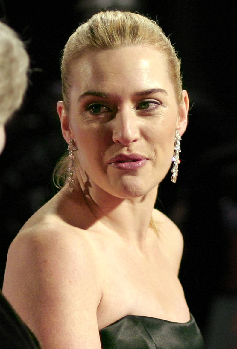 Kate Winslet, hair swept back, in drop earrings and a strapless dark dress, mid-sentence