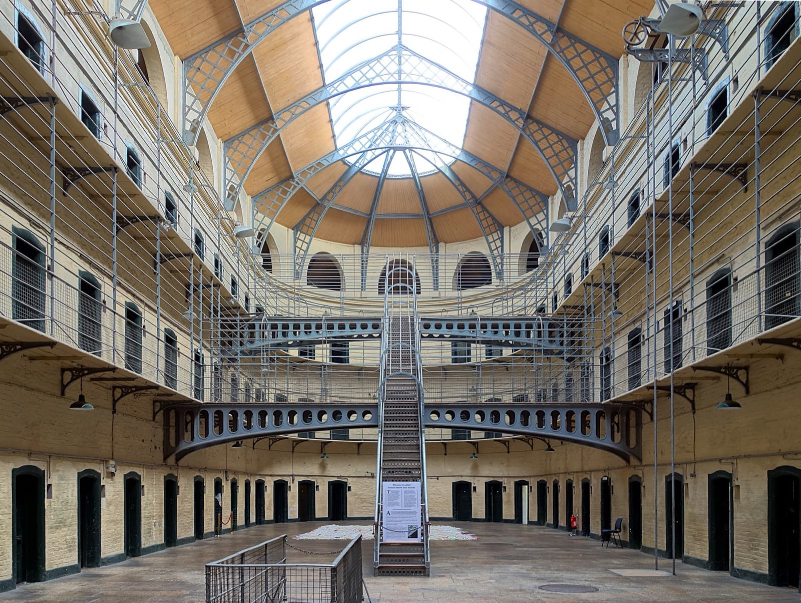 A tall prison hall with three tiers of cell doors, iron walkways and a glass roof