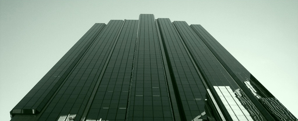 A dark glass office tower seen from below, tinted green