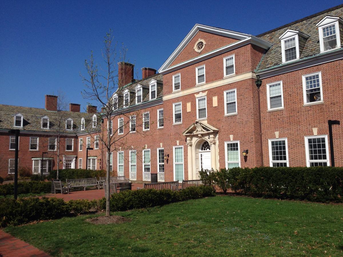 A long three-storey brick residence hall with dormer windows behind a lawn