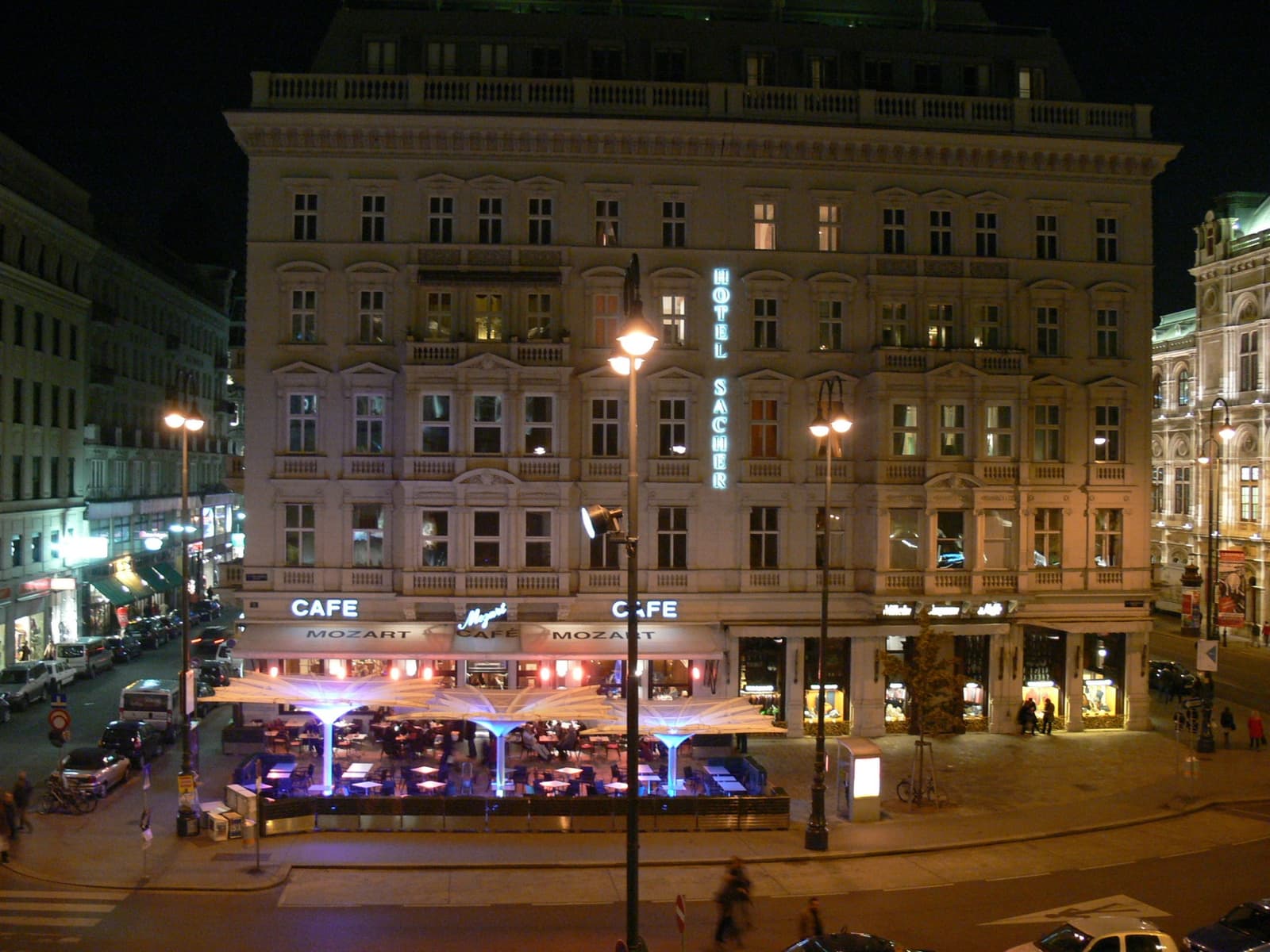 A lit café terrace below a grand hotel front at night