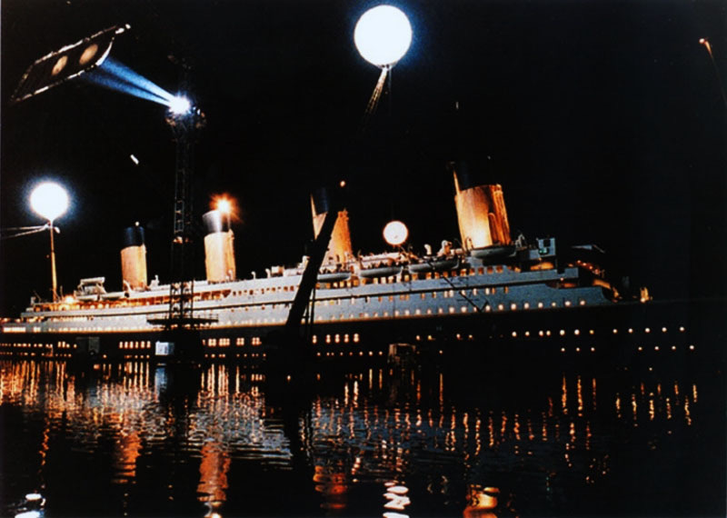 The full-size ship set lit up at night, reflected in the tank, with balloon lights overhead