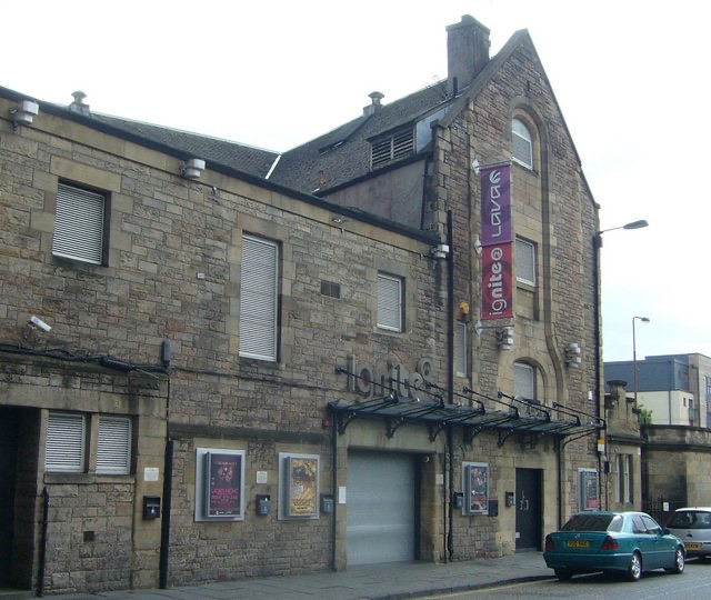 A grey stone club building with a vertical sign on a street corner
