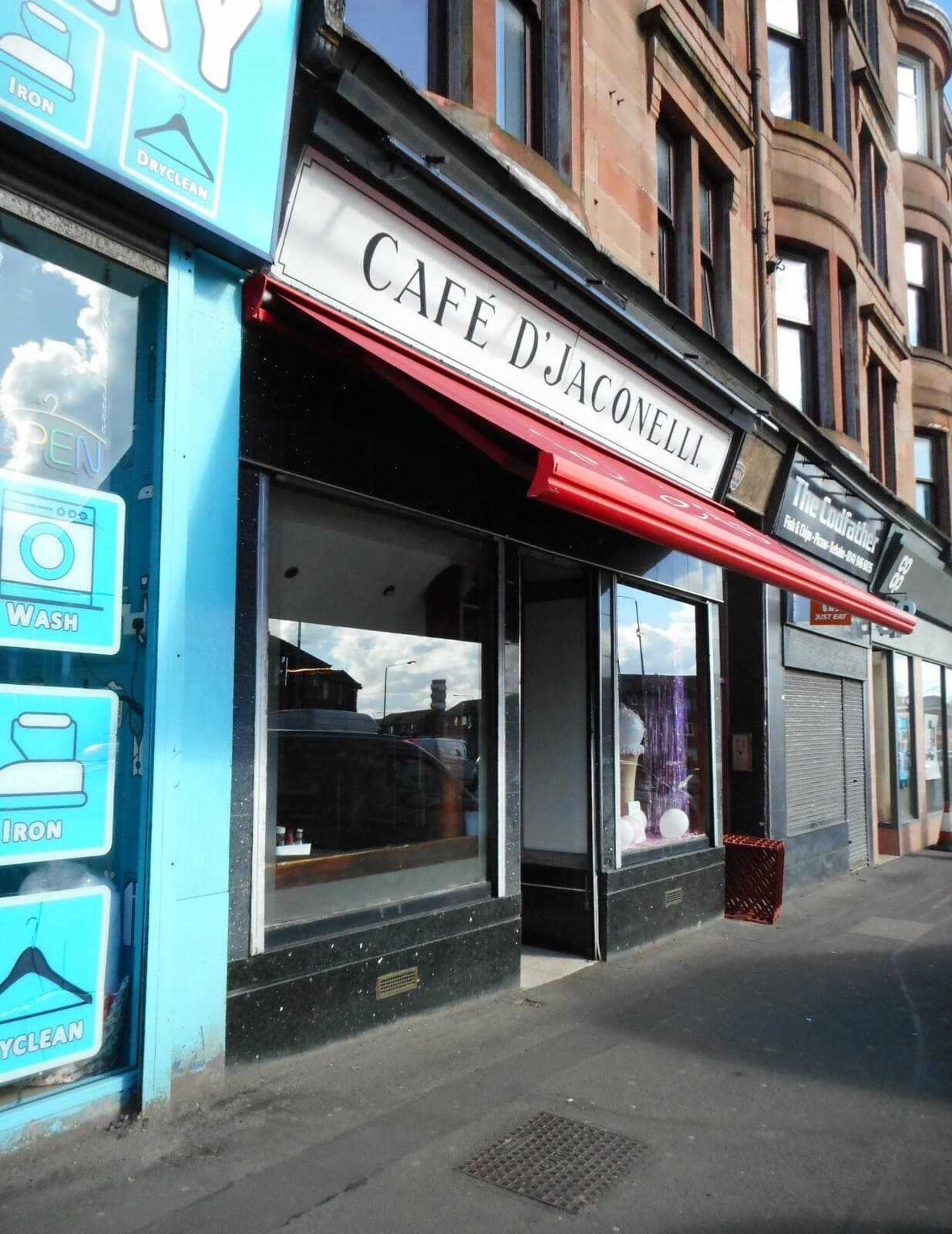 A café front with a red awning and a painted sign reading Cafe D'Jaconelli on a tenement street