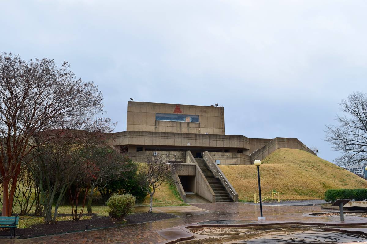 A concrete stage house on a grassy mound with bare trees in front