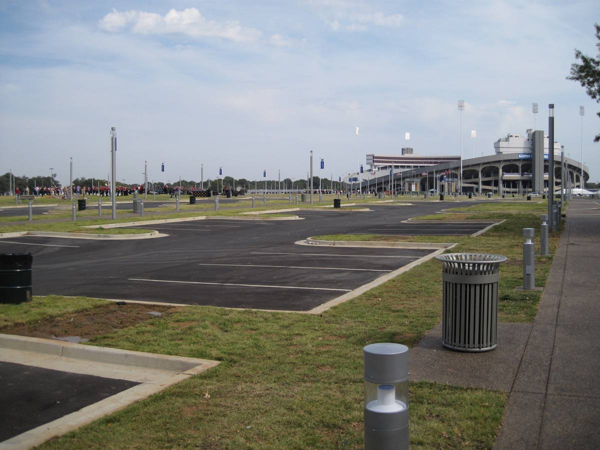 A wide lawn and paved lane leading towards a stadium under a grey sky