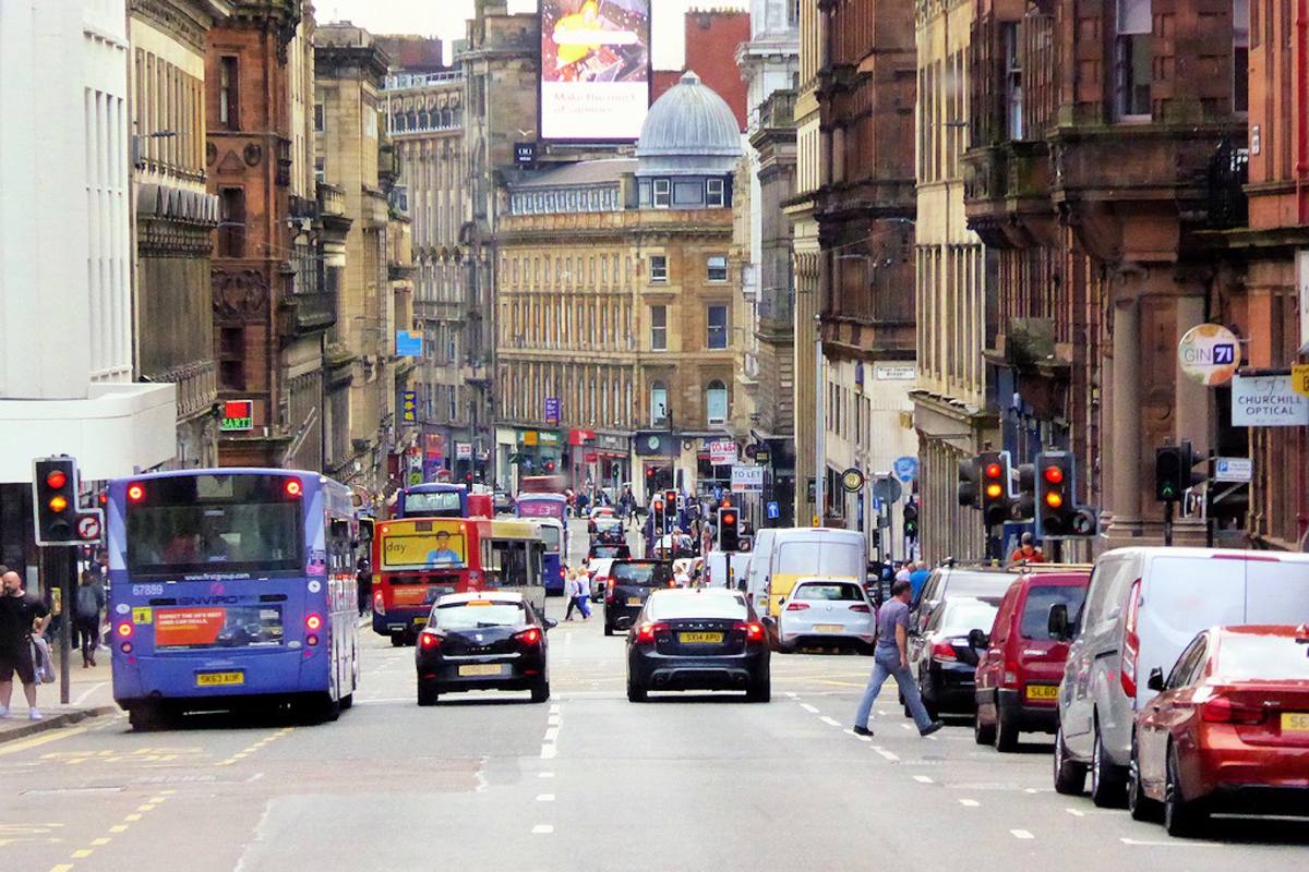 A busy city street of sandstone buildings with buses and cars