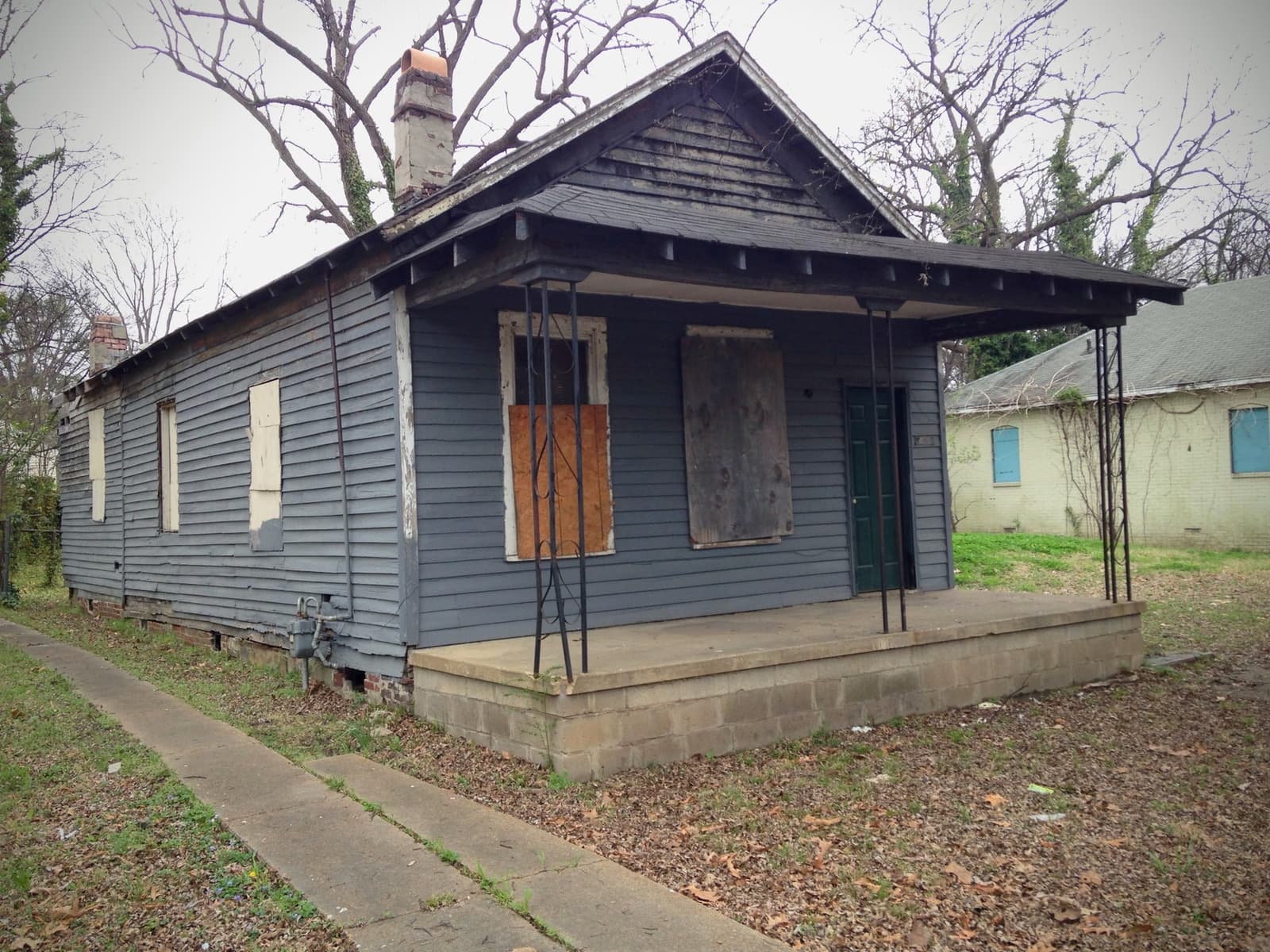 A small boarded-up wooden house with a porch on a Memphis street