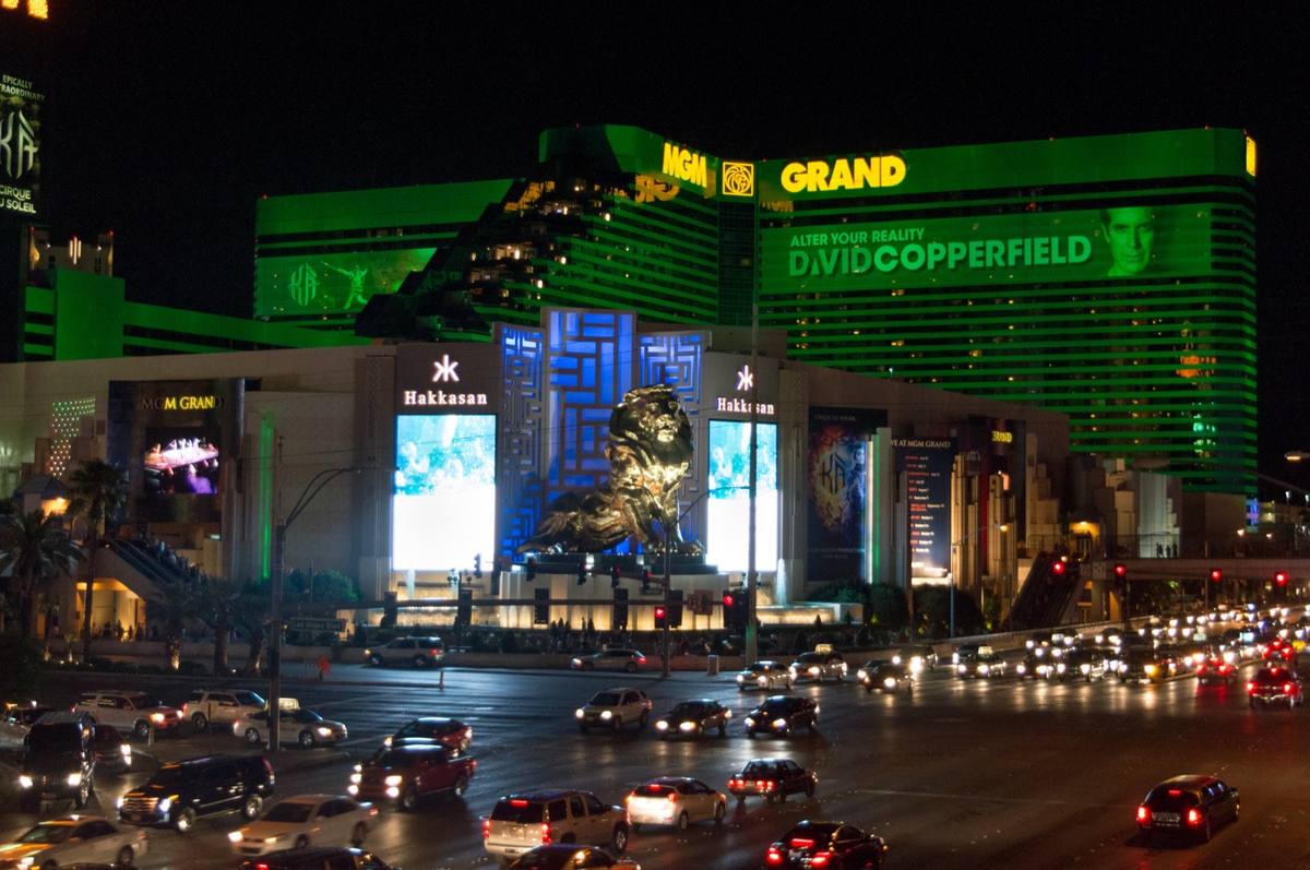 A green-lit hotel tower and its lion statue above traffic at night