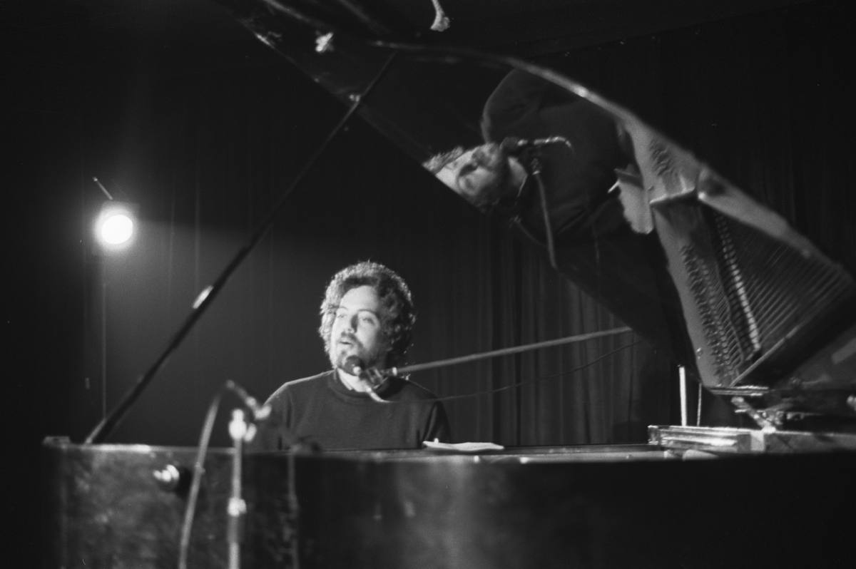 A young Billy Joel playing a grand piano in a darkened room