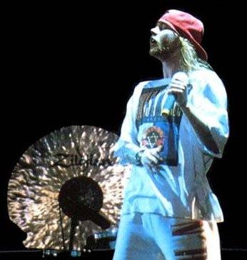 Axl Rose on stage in 1993 in a red cap and white shirt, a large cymbal behind him