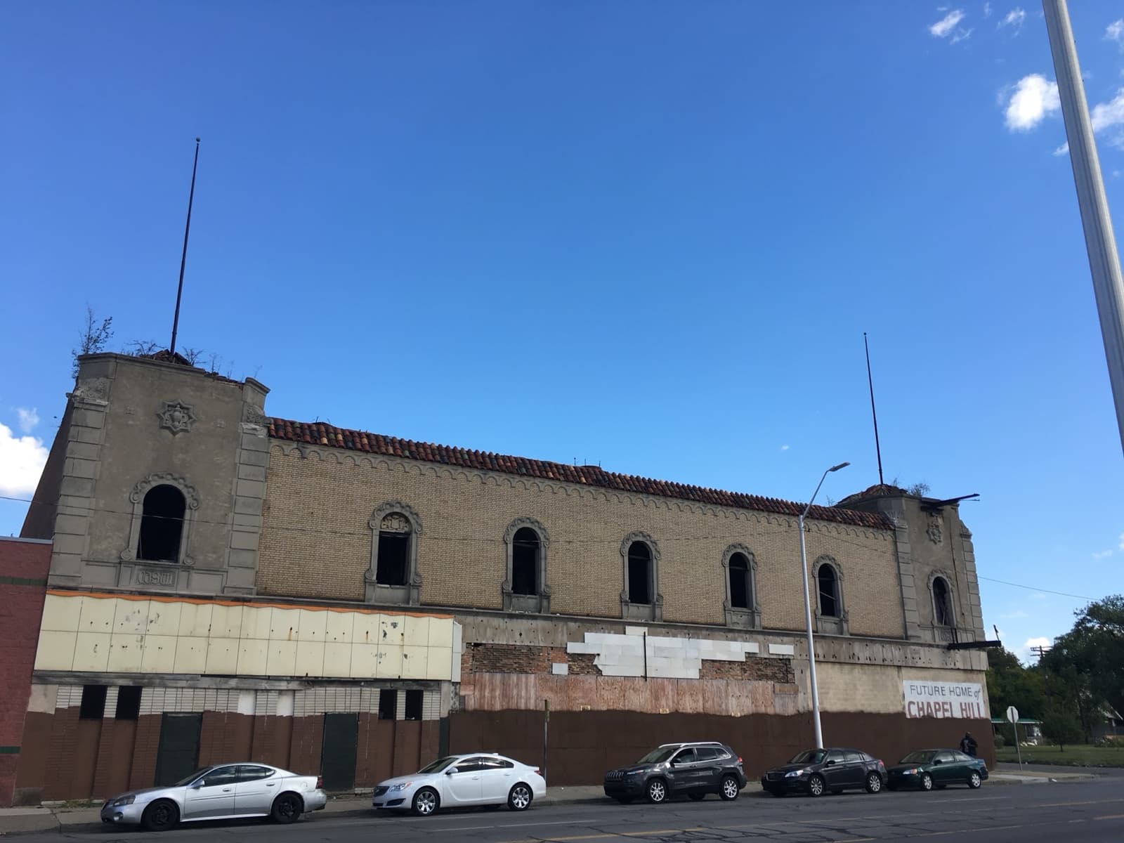 The long, boarded-up brick front of the Grande Ballroom under a blue sky, cars parked along the kerb