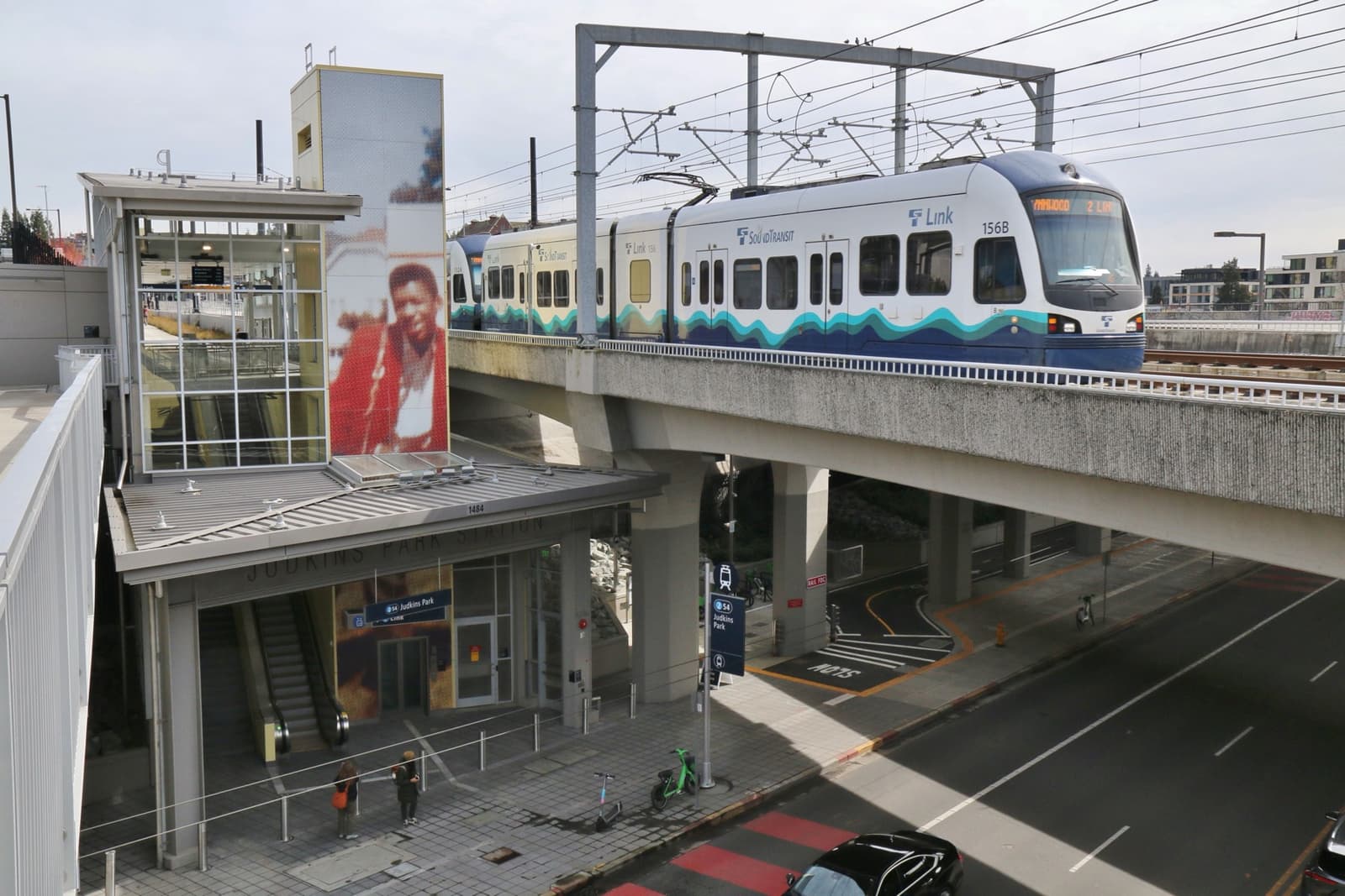 A light-rail station with a tall mural of Hendrix and a train on the bridge