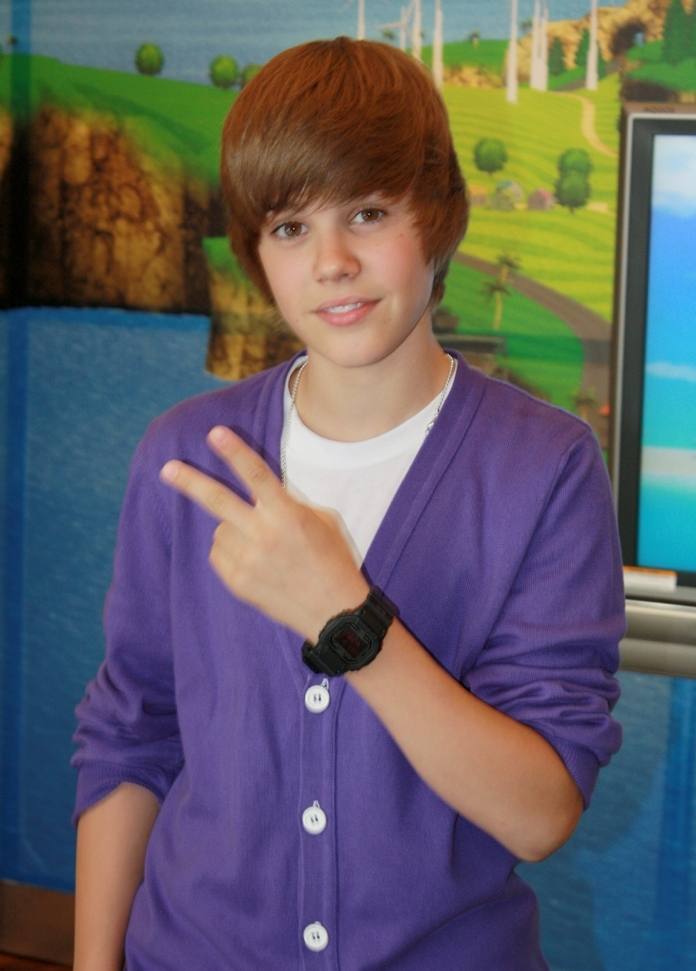 Justin Bieber, aged fifteen, in a purple cardigan, making a peace sign