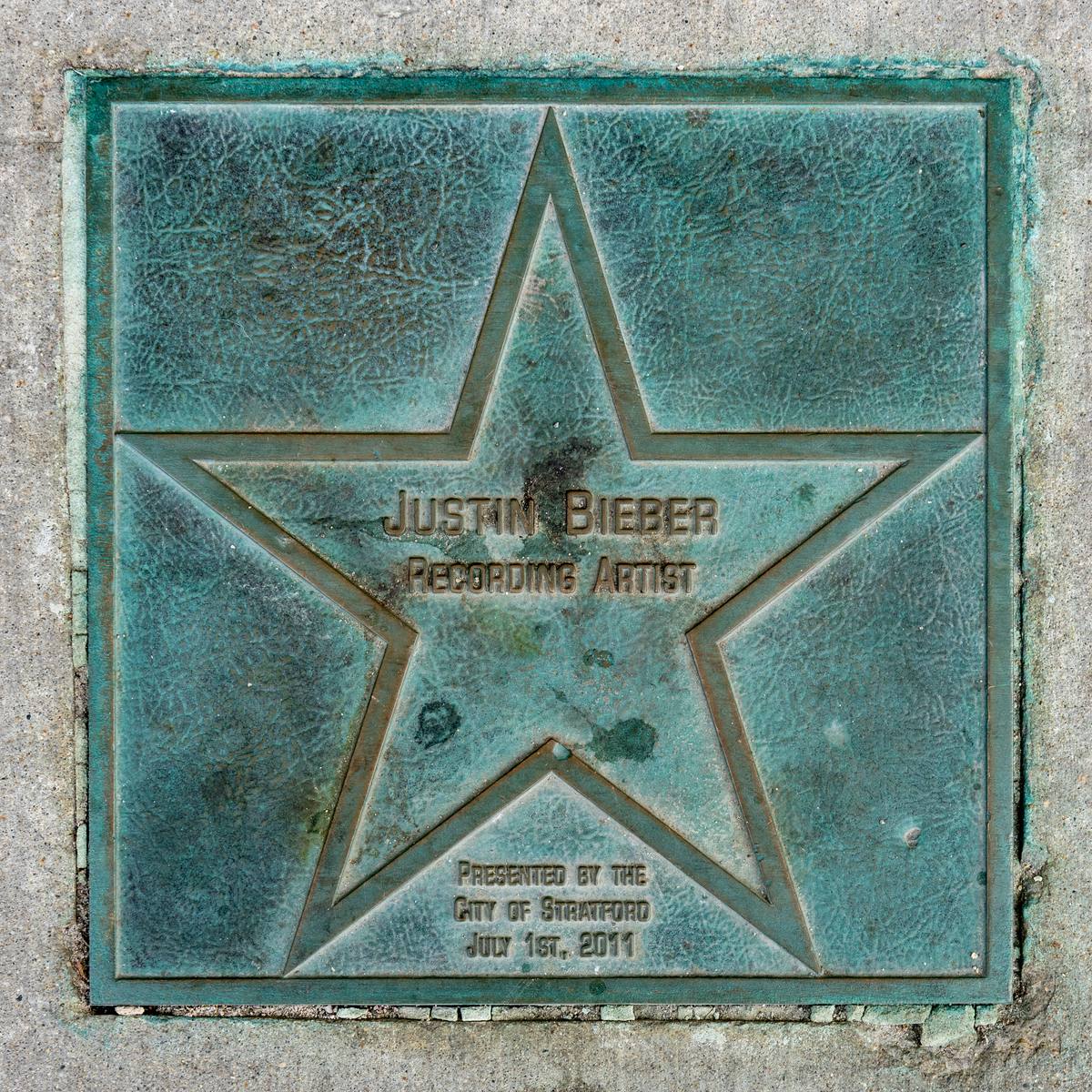 A weathered bronze star plaque set in the pavement, engraved Justin Bieber, Recording Artist