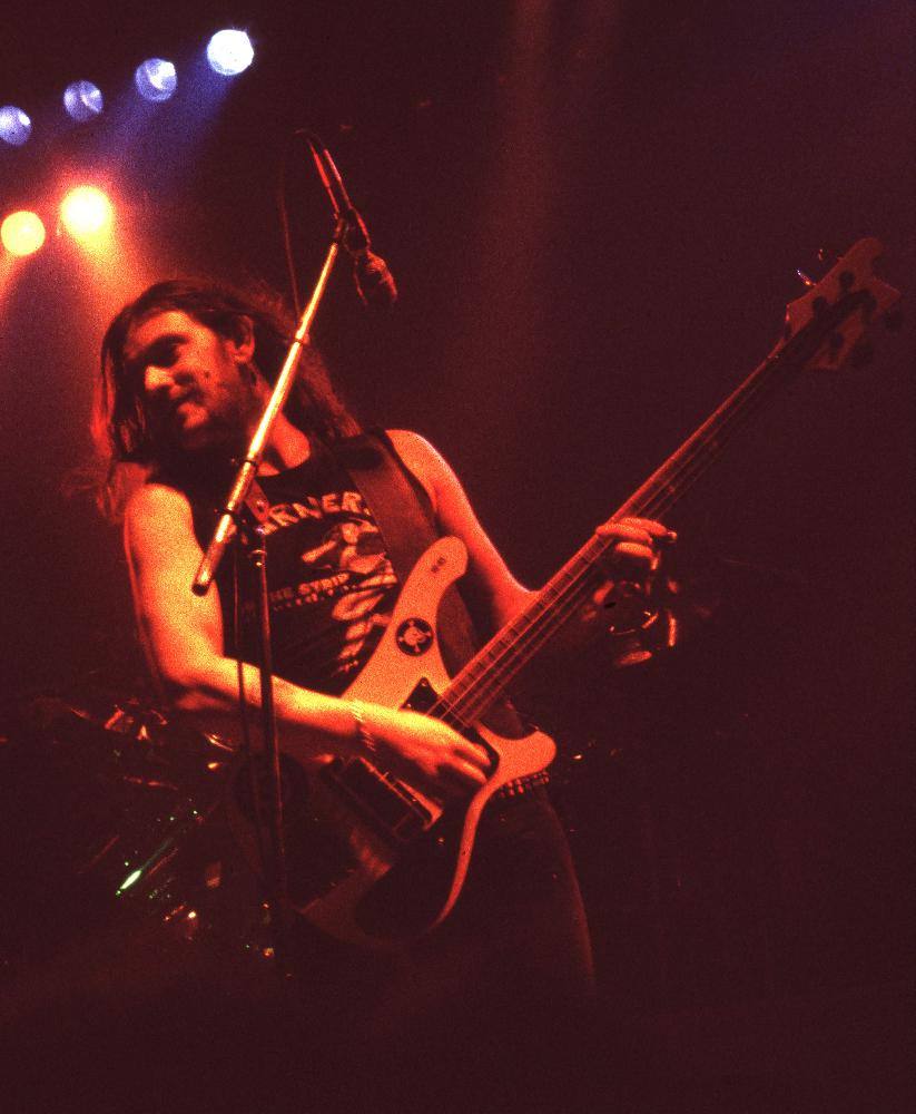 Lemmy singing up into a high microphone with his bass, in 1982